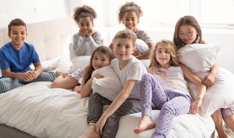 group of tween boys and girls, sitting on a bed and having a safe sleepover or playdate